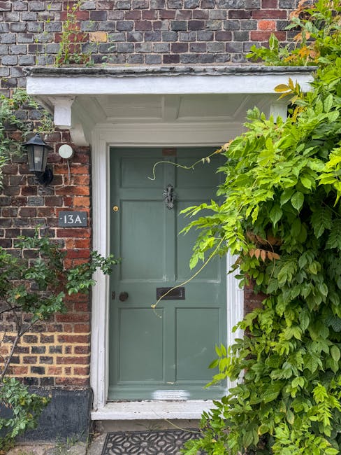 A traditional brick-fronted house with a classic white portico entrance supported by two decorative columns, leading to a dark blue front door. The garden features a stone pathway and steps with yello